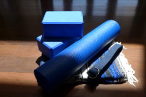 Blue yoga blocks, rolled blue yoga mat, blue yoga sraps, on blue striped yoga blanket