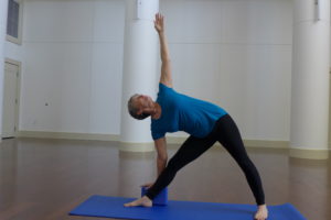 A woman in a turquoise top and black yoga pants practices the yoga triangle position.