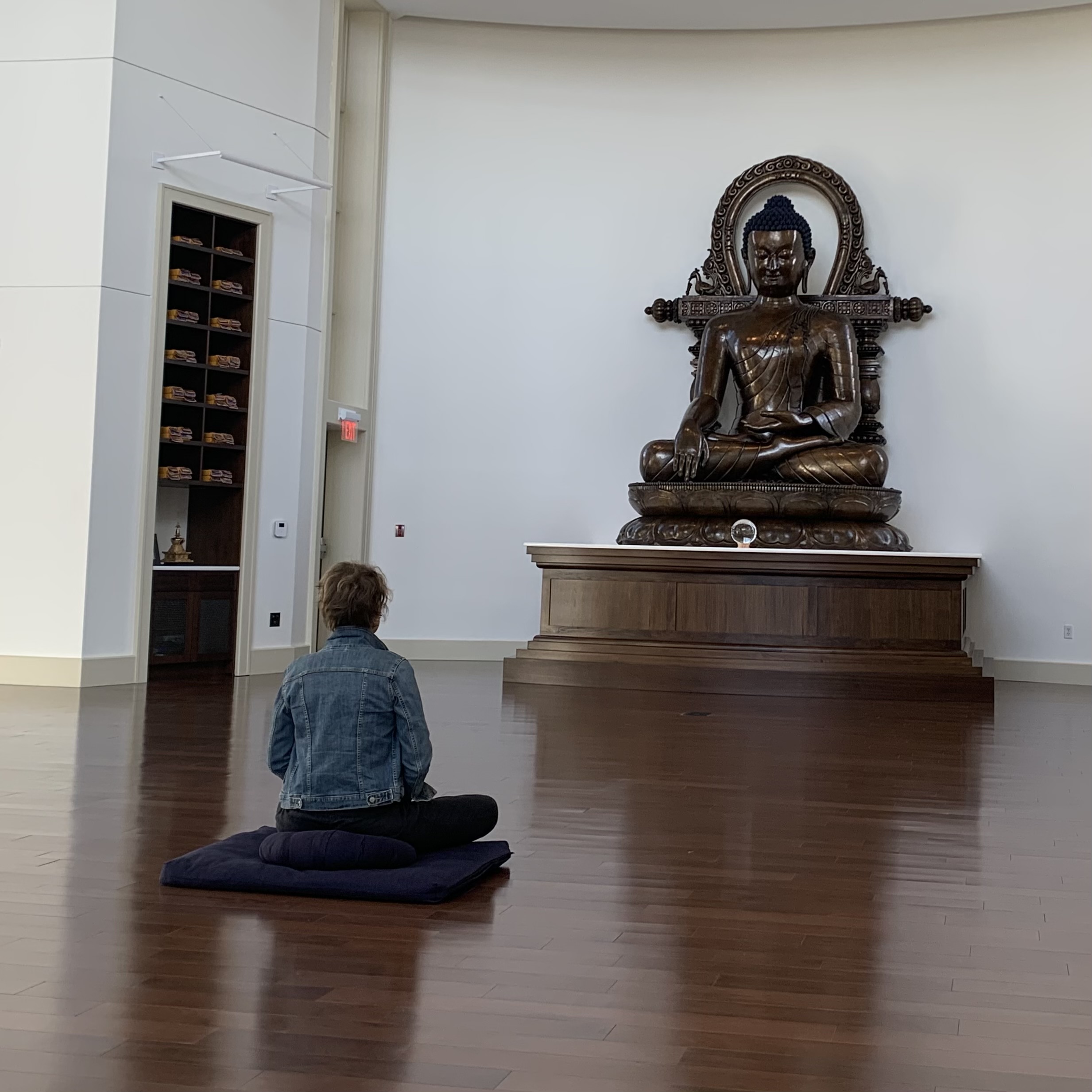 Woman meditating in frotn of a large bronze Buddha
