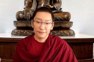 A Buddhist RInpoche inrobes before a statue of Buddha