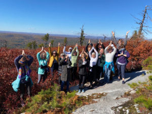 A group of hikers hold a yoga position at the edge of a mountain