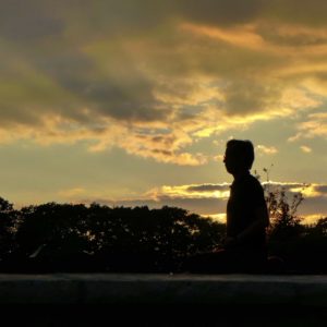 A man meditates silhouetted against the sunset