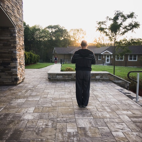 a man stands with his back to the camera in a prayerful pose taking in the morning light