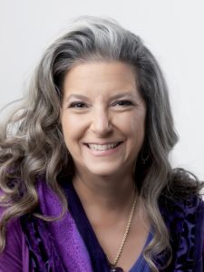 smiling woman with long grey hair and a purple top
