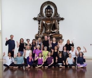 A group of people in yoga clothes wave in front of a Buddha