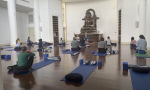 peopel on yoga mats in front of a large Buddha
