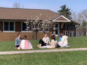 A group of people laugh on the lawn with a dogwood tree in bloom behind